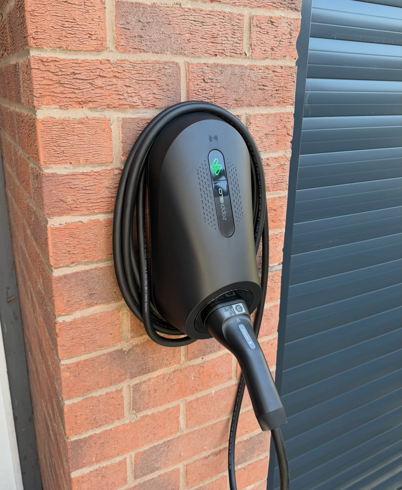 Tethered myenergi zappi EV charger installed beside a garage door