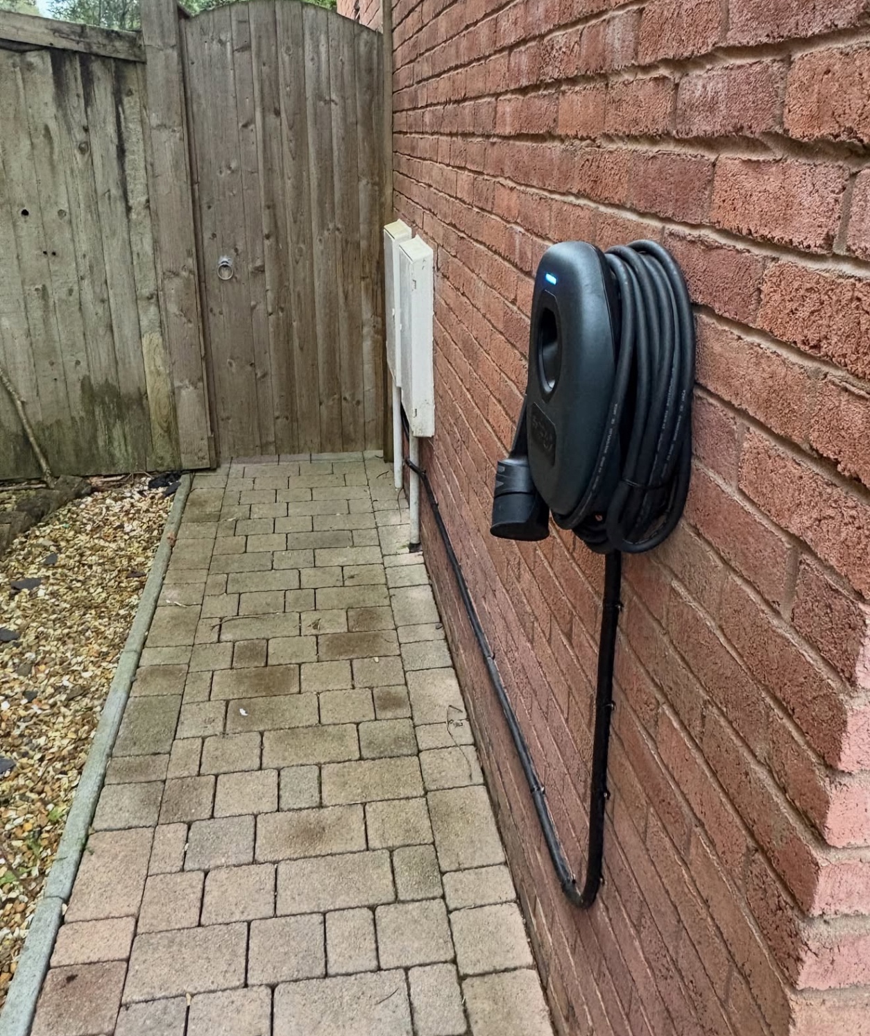 Tethered black EV charger installed beside a paved driveway