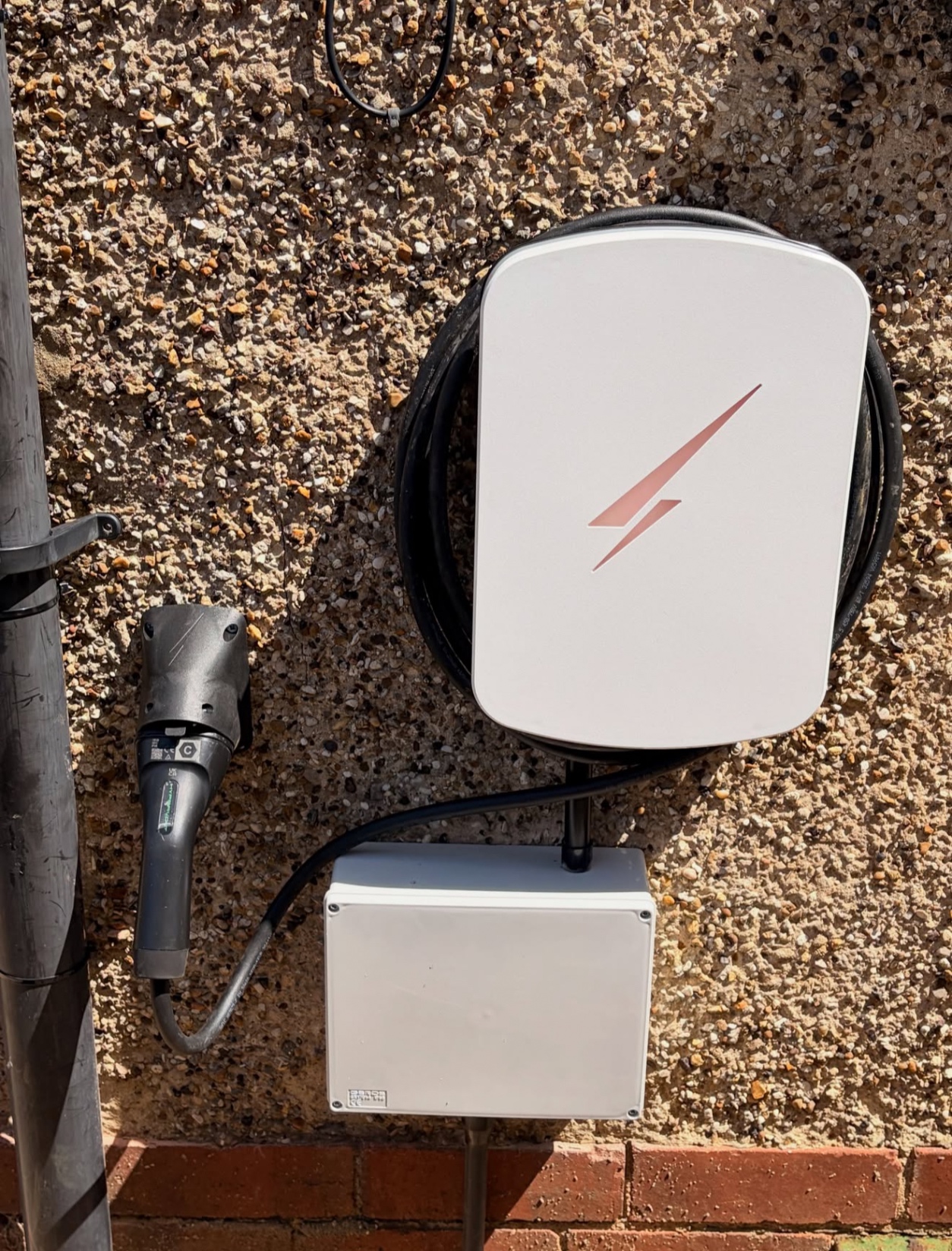 White tethered EV charger installed on a textured exterior wall
