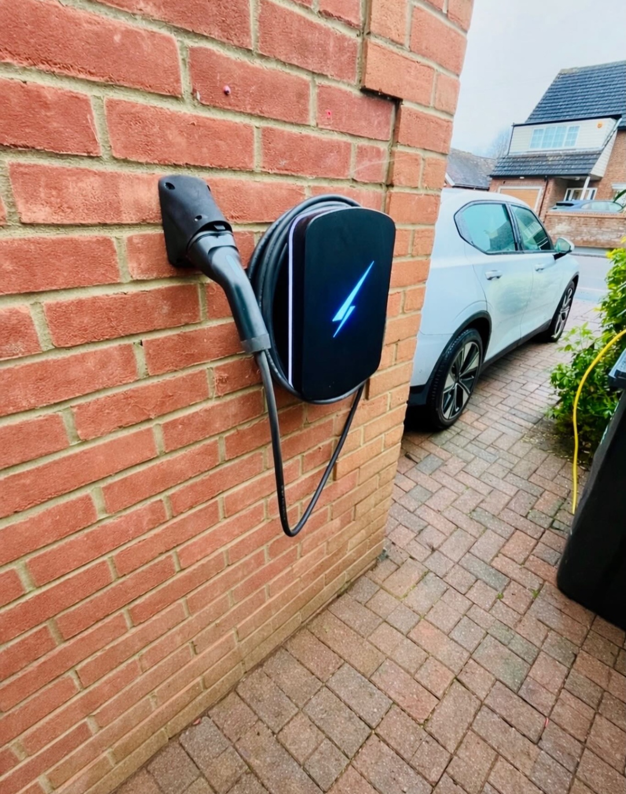Tethered EV charger installed on a brick house beside a driveway