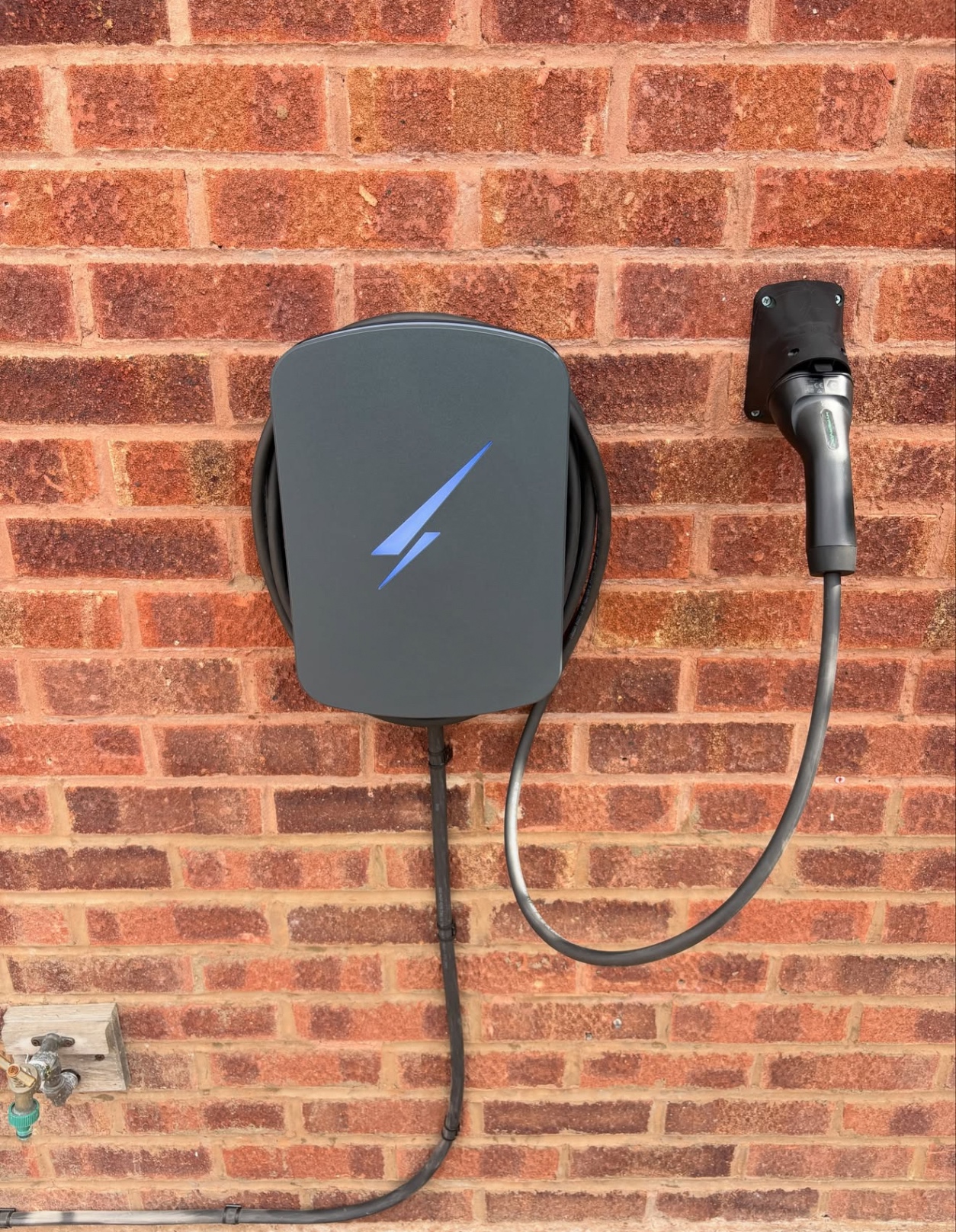 Tethered EV charger and cable holster installed on a red brick wall